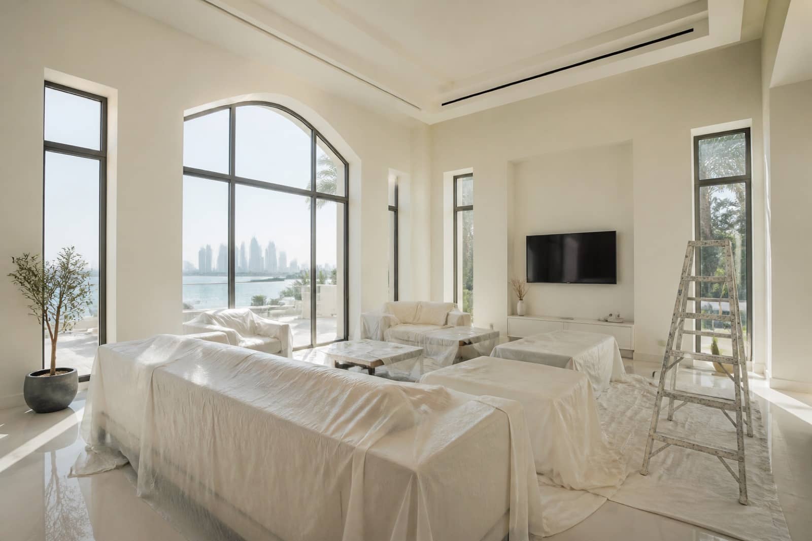 Spacious villa living room in Dubai prepared for painting, with covered furniture and a ladder