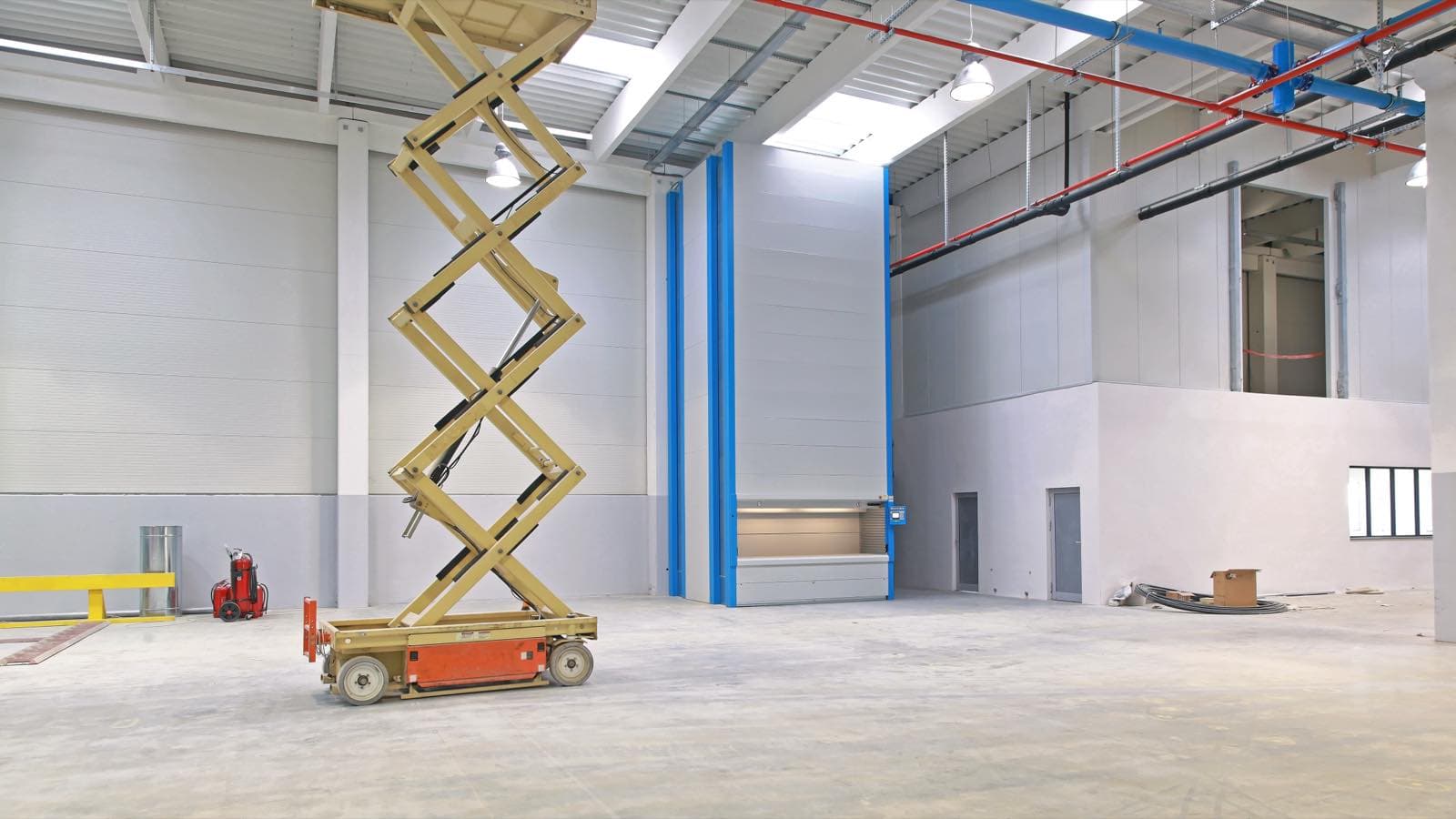 Warehouse Wall and Ceiling Painting in Dubai: Empty warehouse hall with a scissor lift ready for wall and ceiling painting