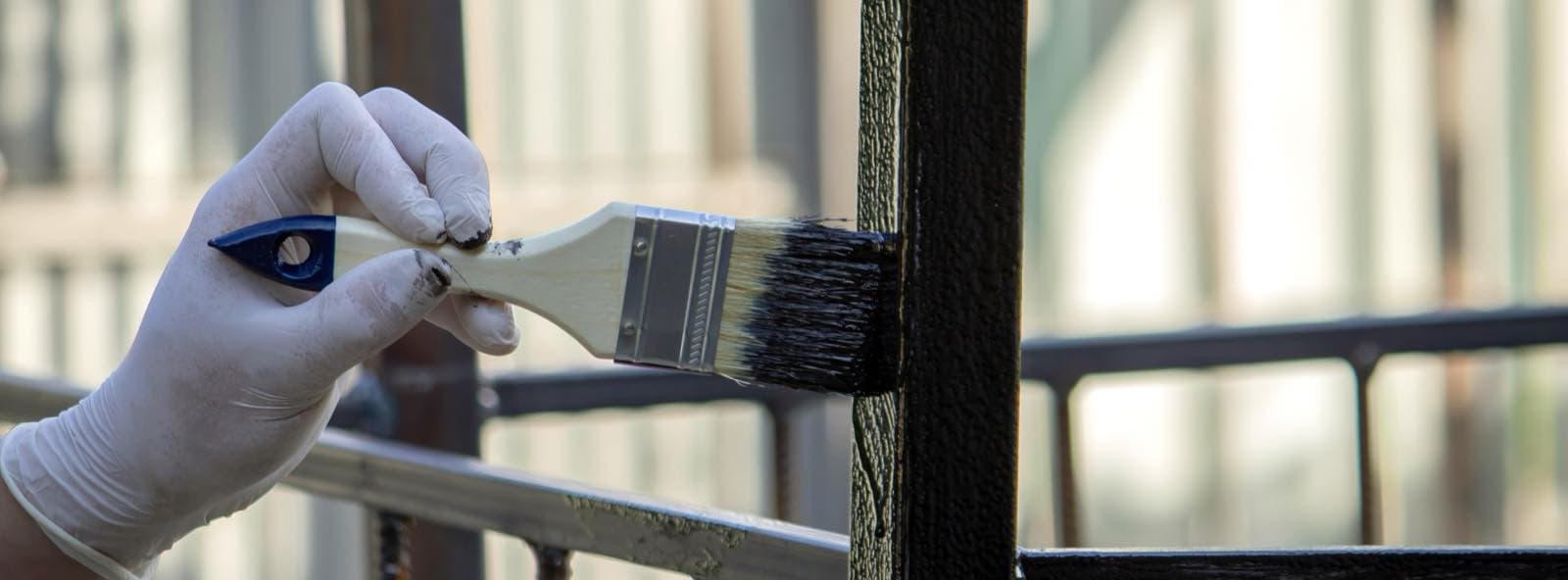 Balcony and Parapet Painting in Dubai: Gloved hand painting a black balcony railing with a brush