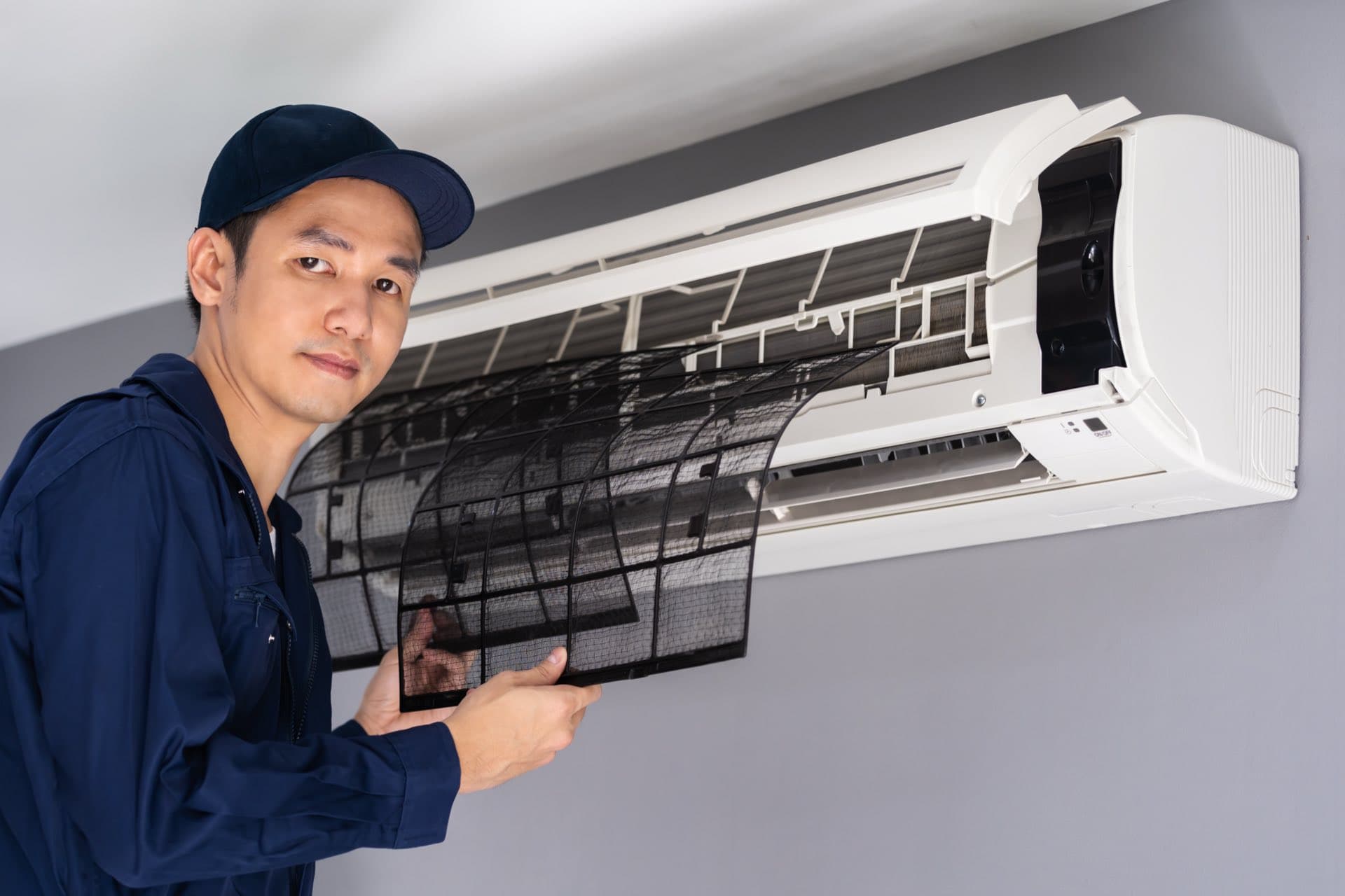 AC Filter and Drain Check in Dubai: Technician removing the air filter from a wall-mounted split AC