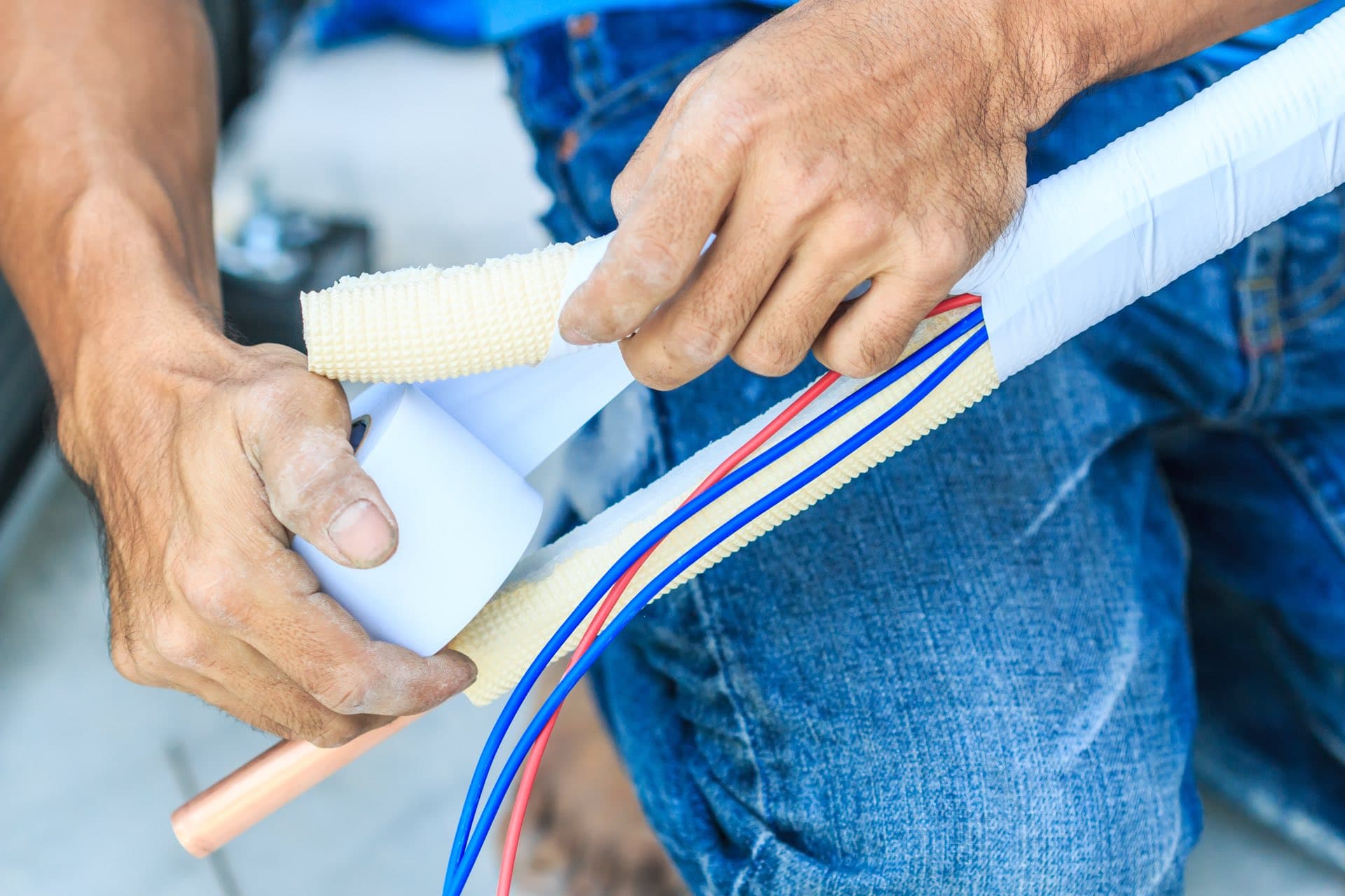 AC Pipework and Electrical Connection in Dubai: Hands taping insulated copper pipes and wiring for an AC installation