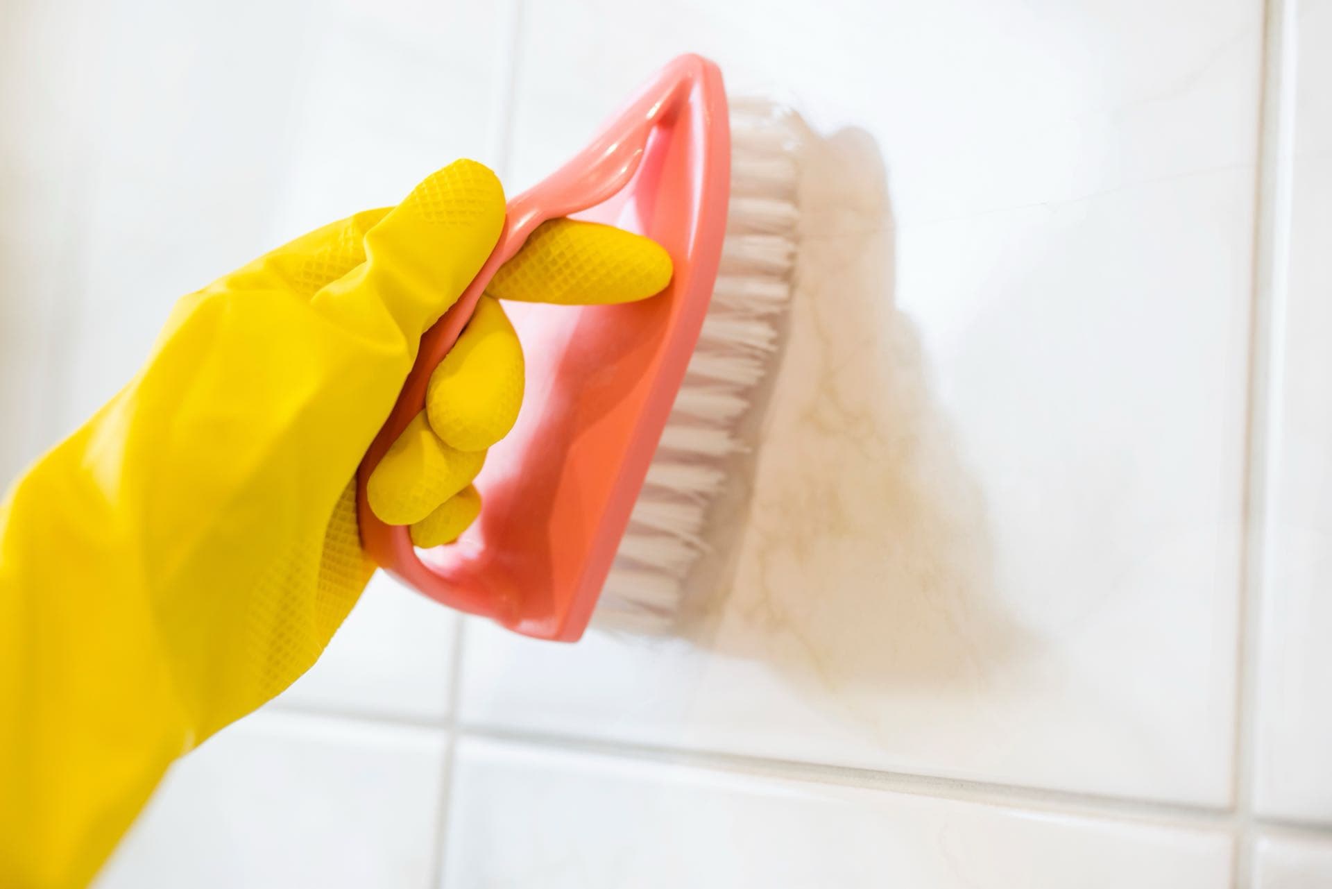 Bathroom Deep Cleaning in Dubai: Gloved hand scrubbing bathroom wall tiles with a brush