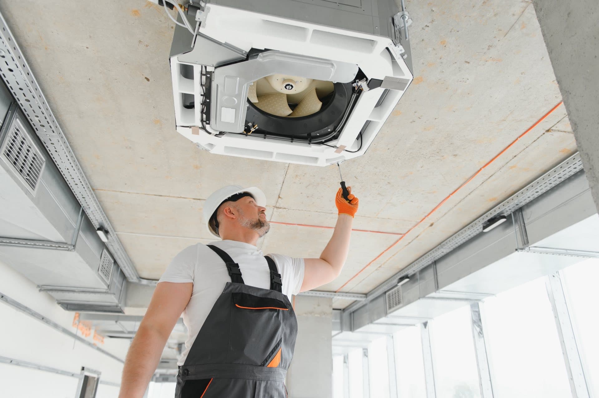 Central AC System Repair in Dubai: Technician in a hard hat servicing a ceiling-mounted AC unit in a Dubai building