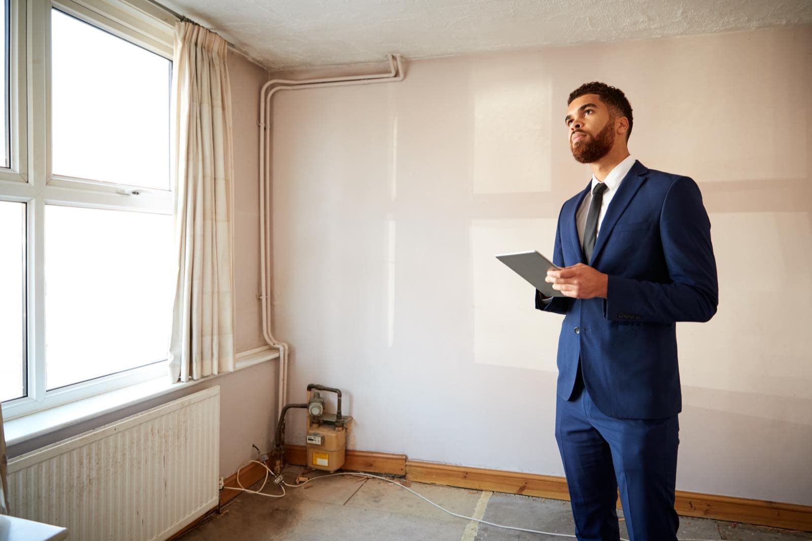 Remote Owner Coordination in Dubai: Property agent in a suit with a tablet inspecting an empty apartment room