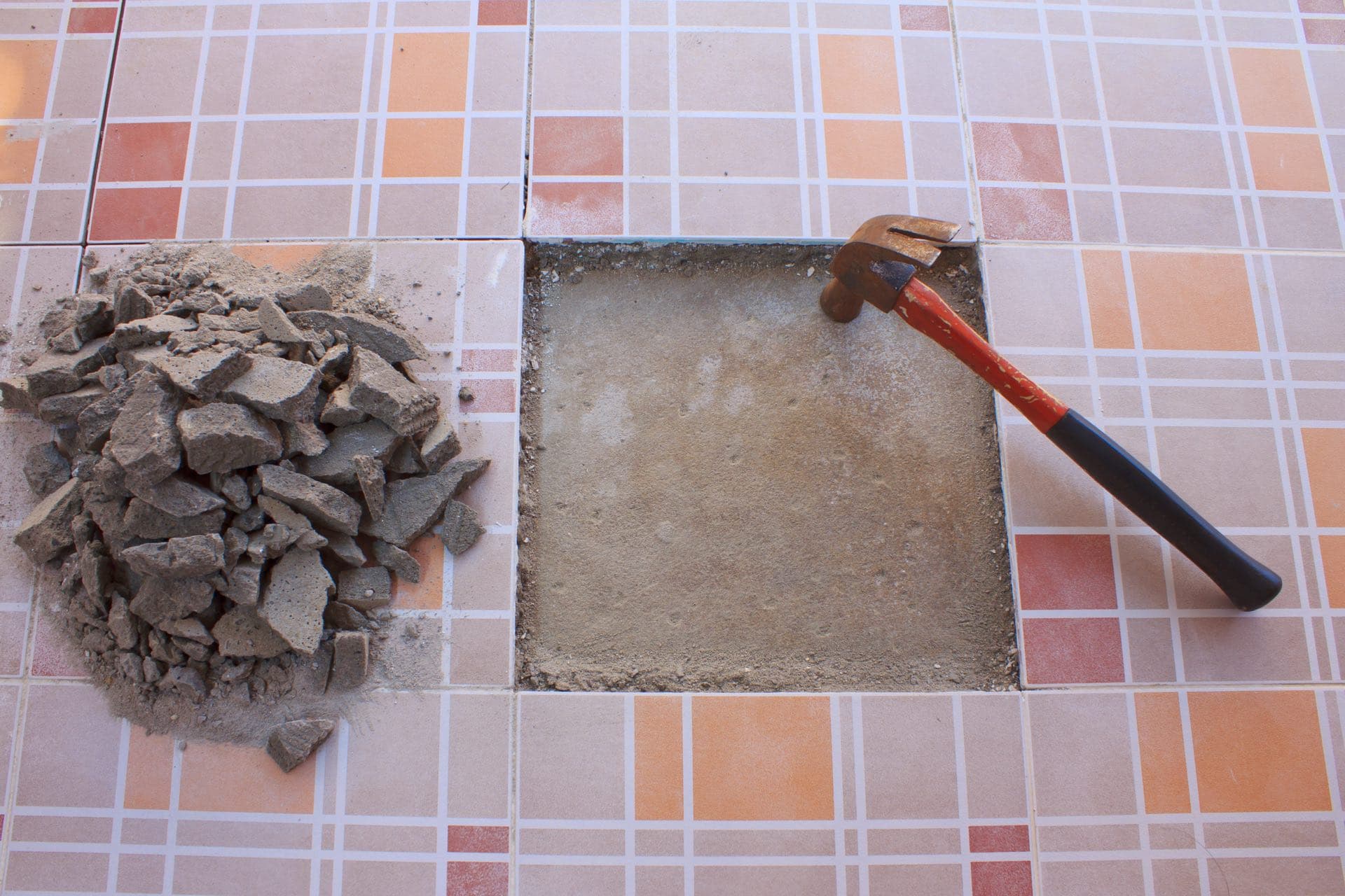 Tile Replacement and Repair in Dubai: One floor tile cut out with a chisel and hammer beside a pile of rubble
