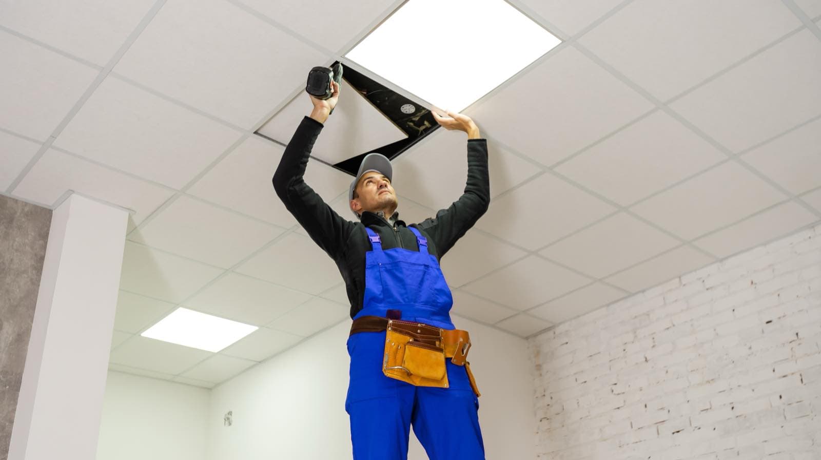 Out-of-Hours Scheduled Work in Dubai: Technician in blue overalls reaching into an office ceiling to work on the lighting