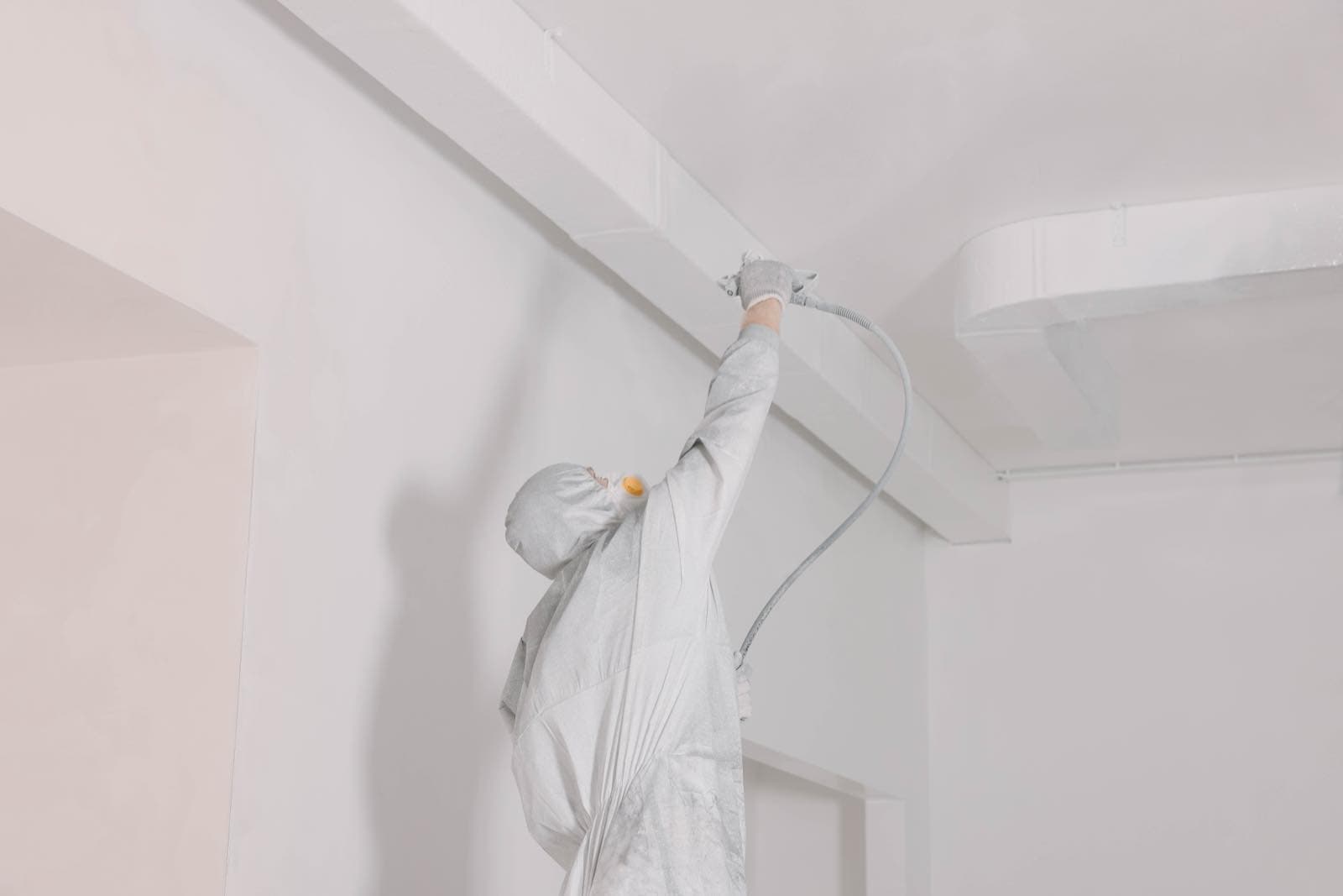 Wall and Ceiling Spraying in Dubai: Painter in a protective suit spraying a ceiling with a spray gun indoors