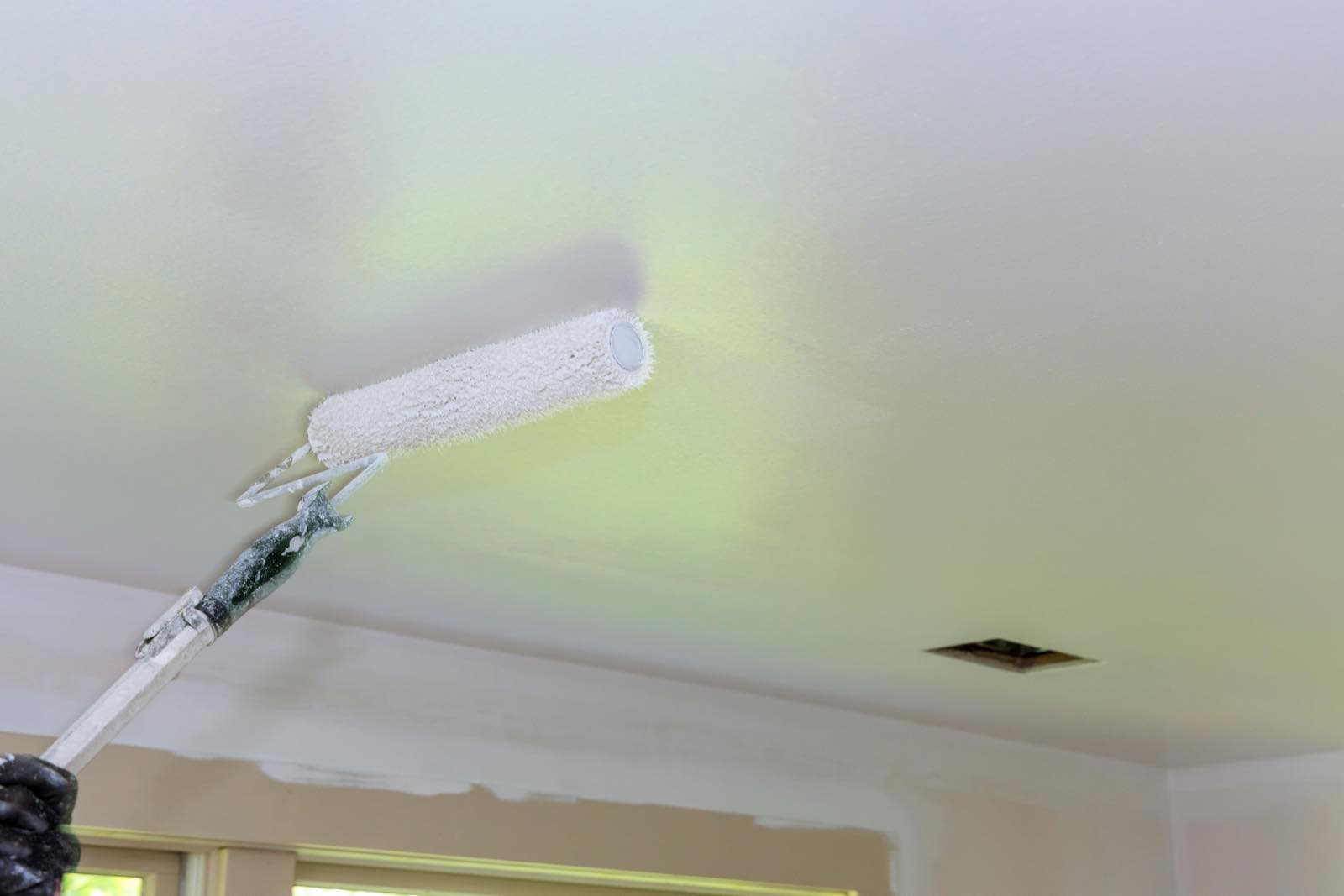 Ceiling and Stain Repainting in Dubai: Painter rolling paint onto a ceiling with an extension pole