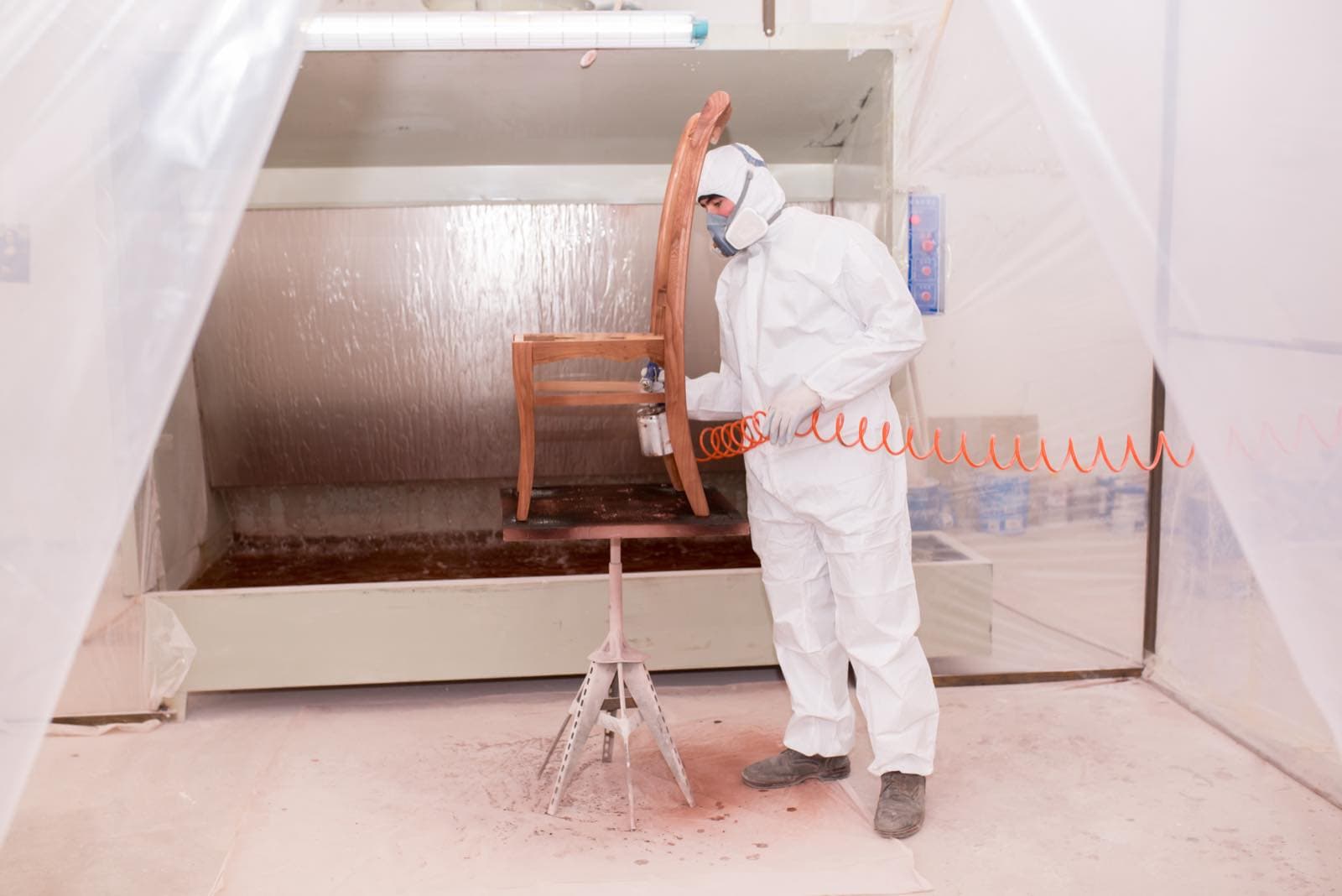 Furniture and Joinery Spraying in Dubai: Worker in overalls spraying a wooden chair in a paint booth