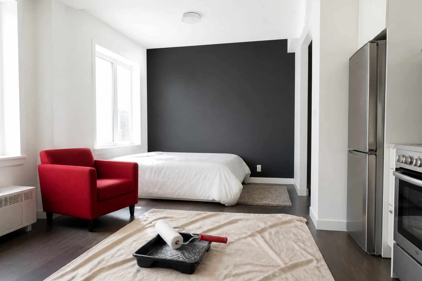 Compact studio apartment with a dark feature wall, a red armchair and a paint tray on a drop cloth