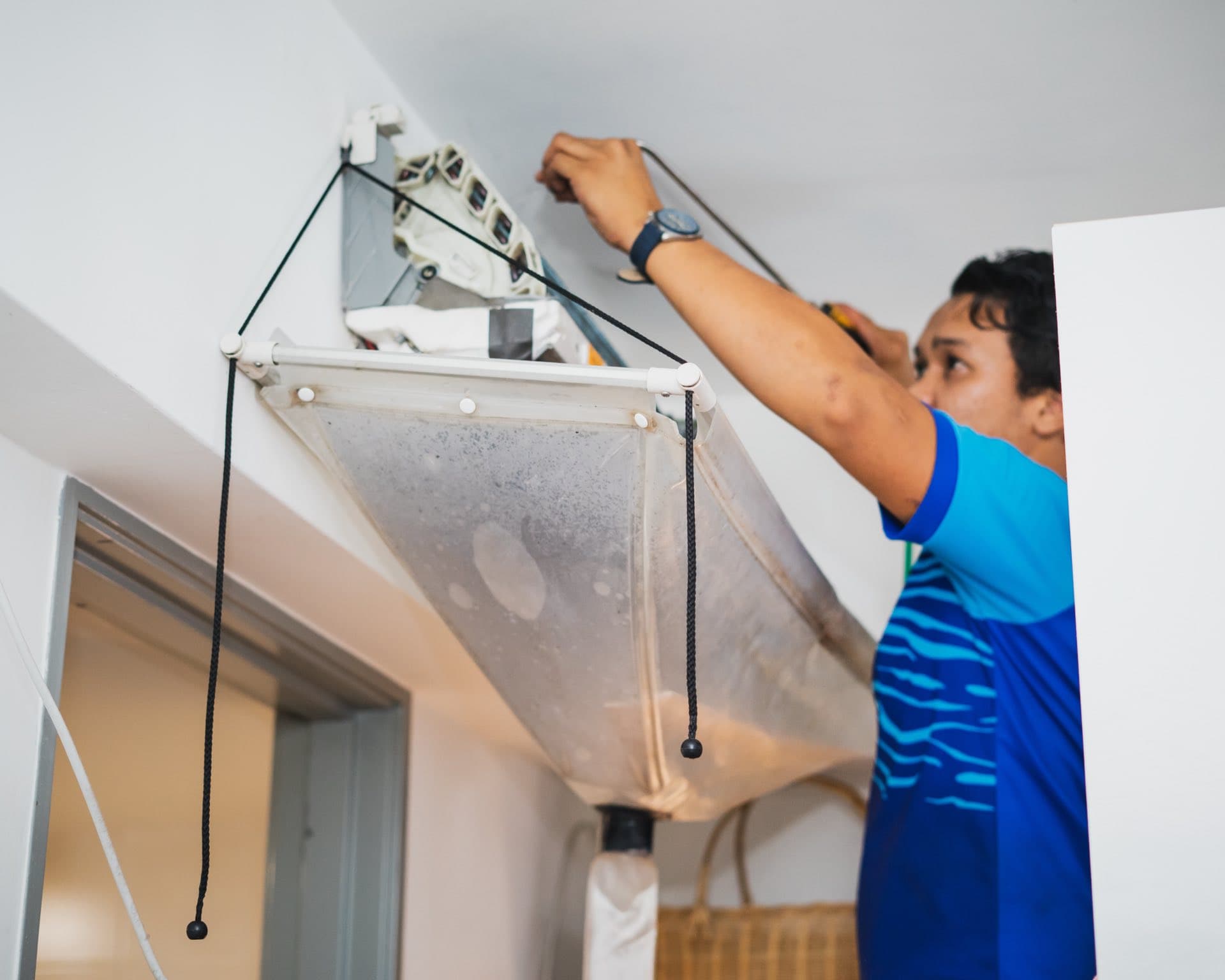 AC Drain Line Clearing in Dubai: Technician cleaning a split AC with a collection bag catching the water