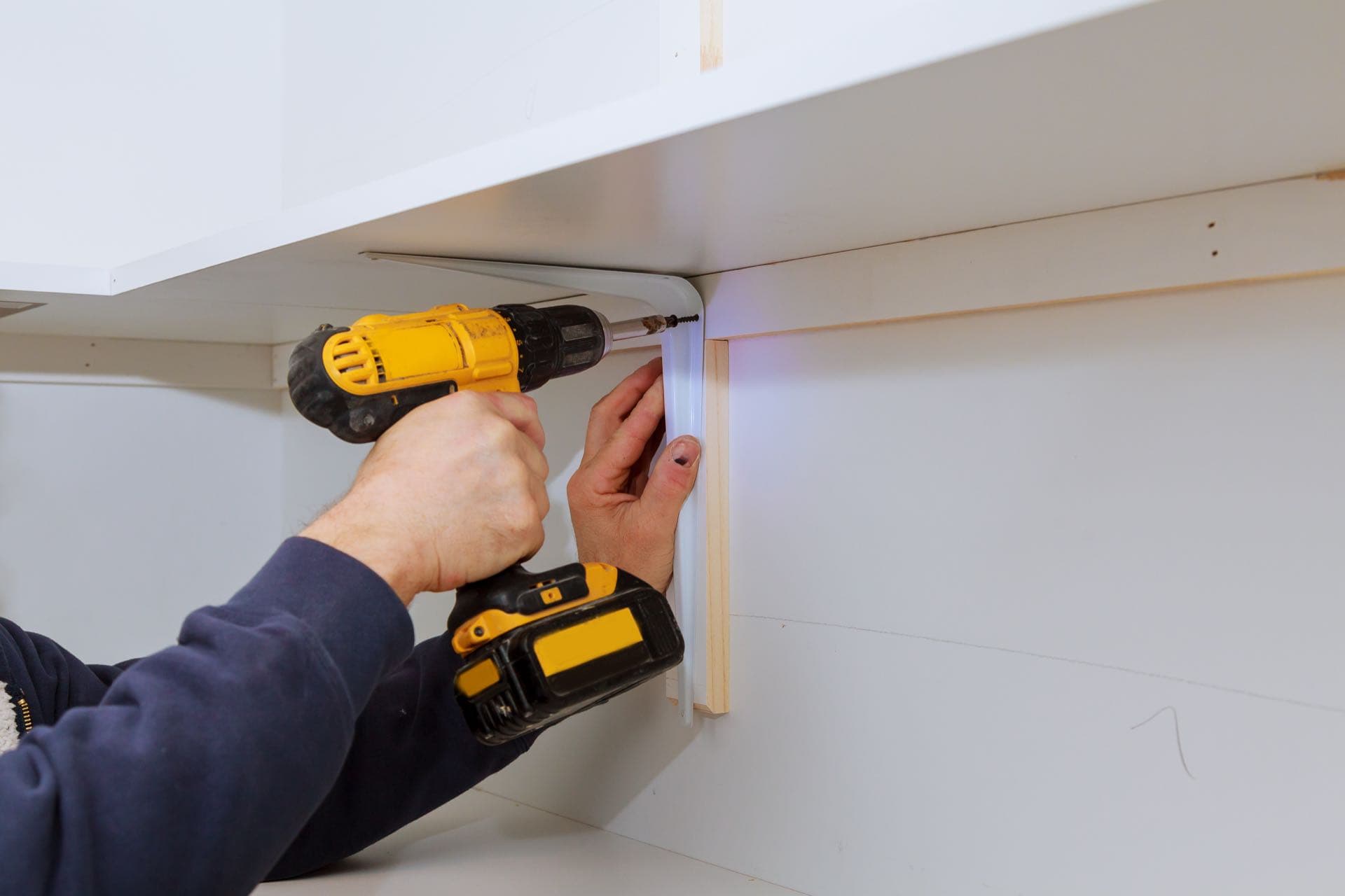 Furniture Wall Fixing in Dubai: Hands drilling a shelf bracket into a wall