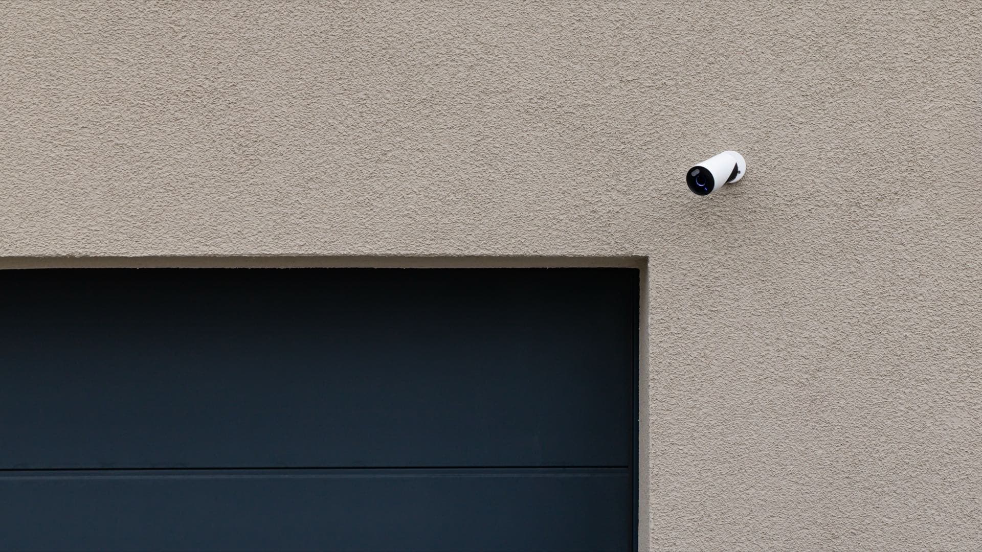 Home CCTV Installation in Dubai: White security camera mounted on a house wall above a garage door in Dubai