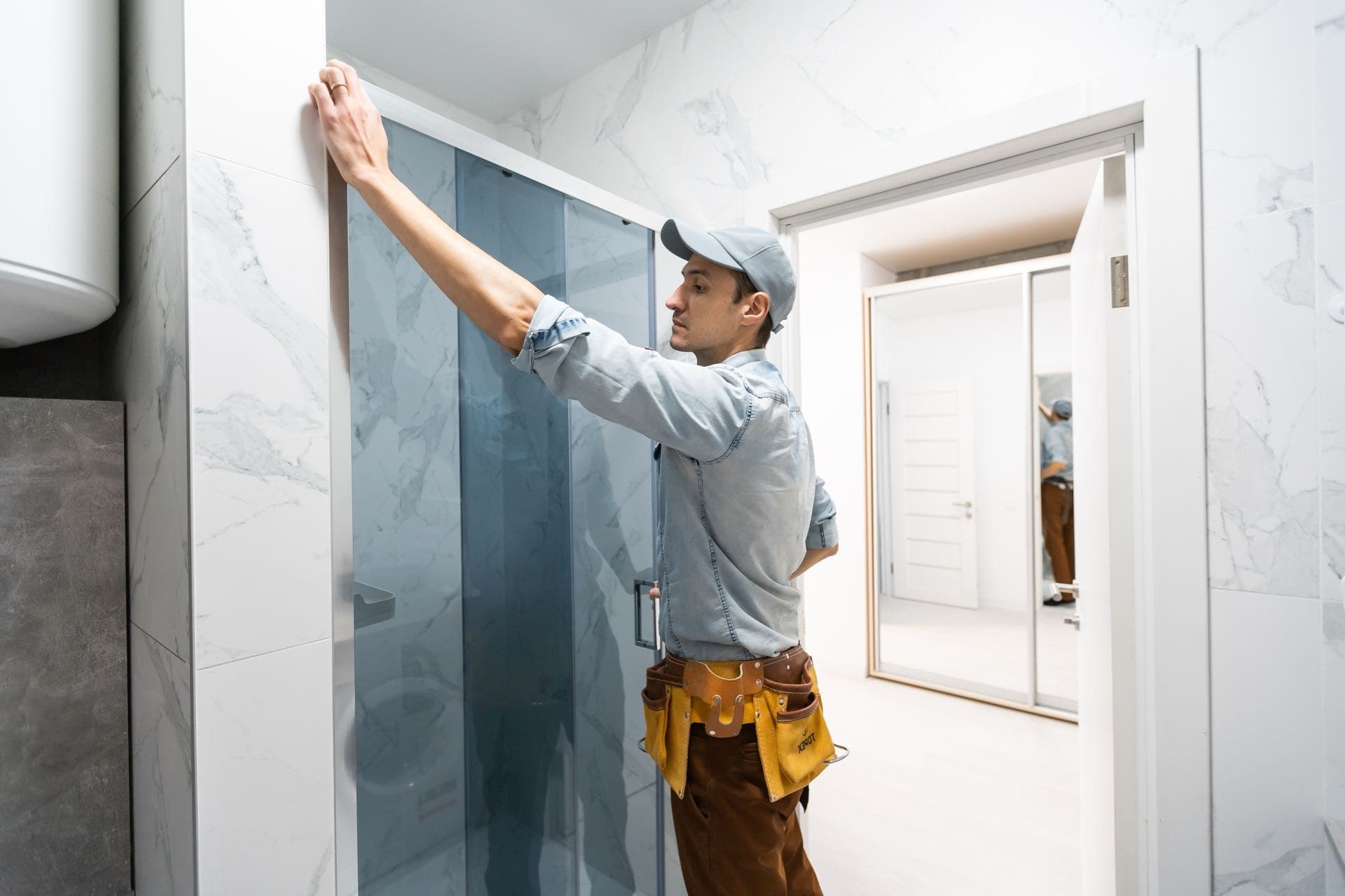 Shower Screens and Mirrors in Dubai: Installer fitting a glass shower door on an enclosure
