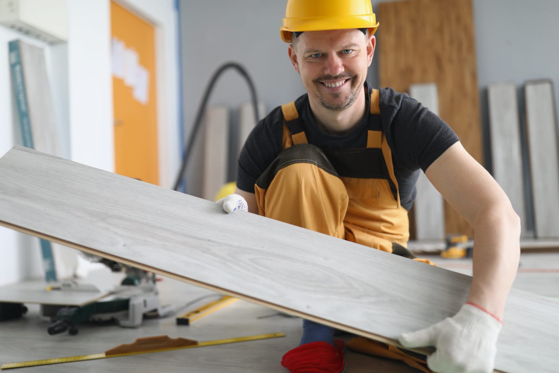 Flooring and Finishing in Dubai: Smiling worker in a hard hat laying a laminate floor plank