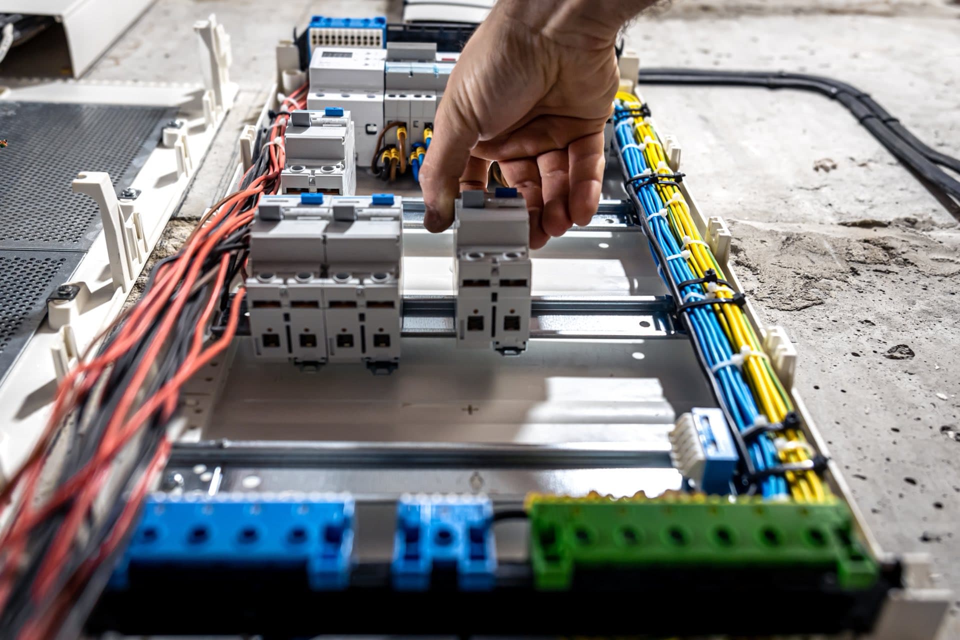 إصلاح أسلاك اللوحة والدوائر في دبي: يد تعمل على القواطع والأسلاك داخل لوحة توزيع